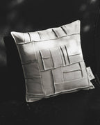 Coussin carré ivoire à reliefs géométriques façon briques, étiquette latérale visible.