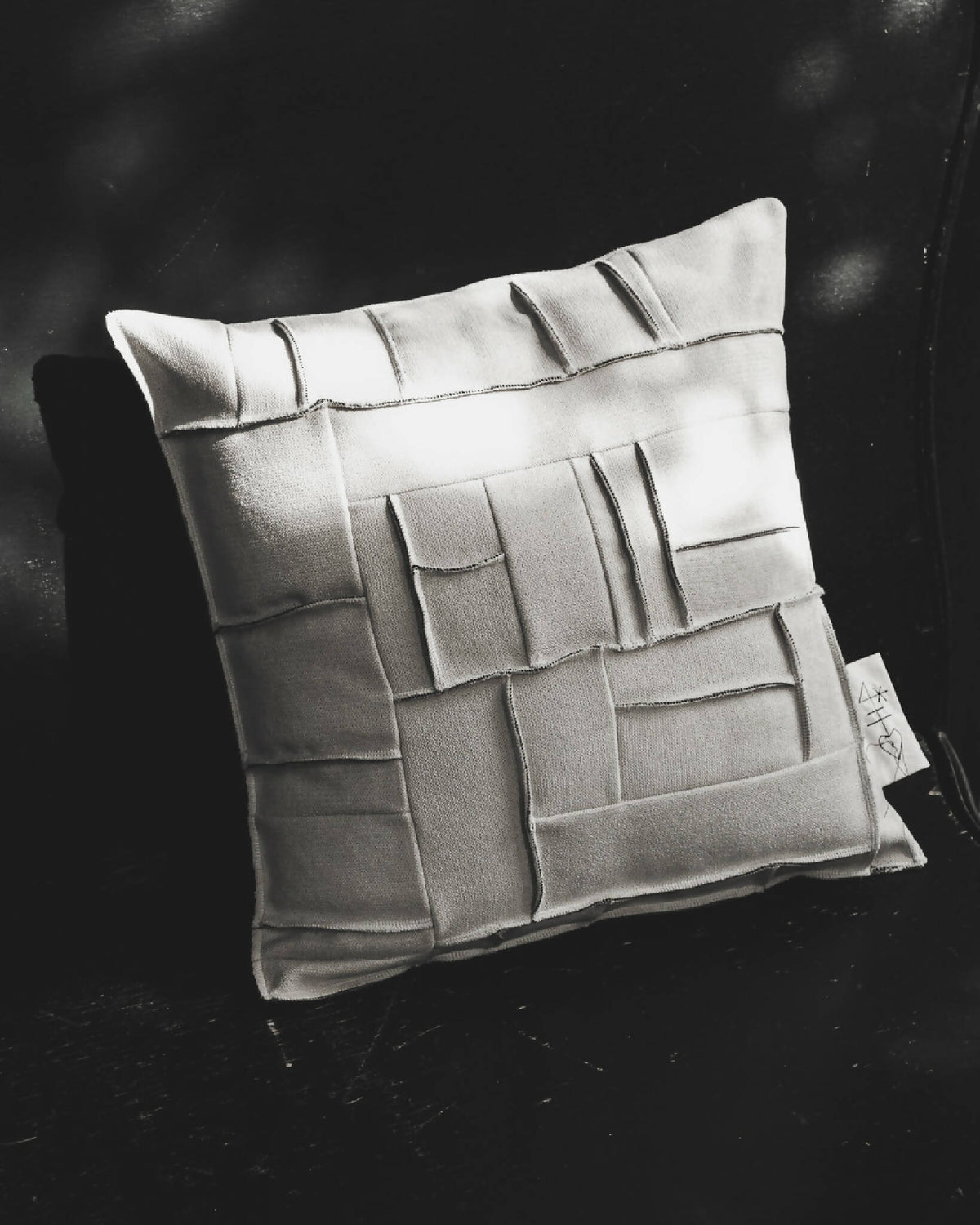 Coussin carré ivoire à reliefs géométriques façon briques, étiquette latérale visible.