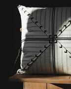 Coussin rectangulaire à rayures bleu-gris, motifs fléchés noirs et point central.
