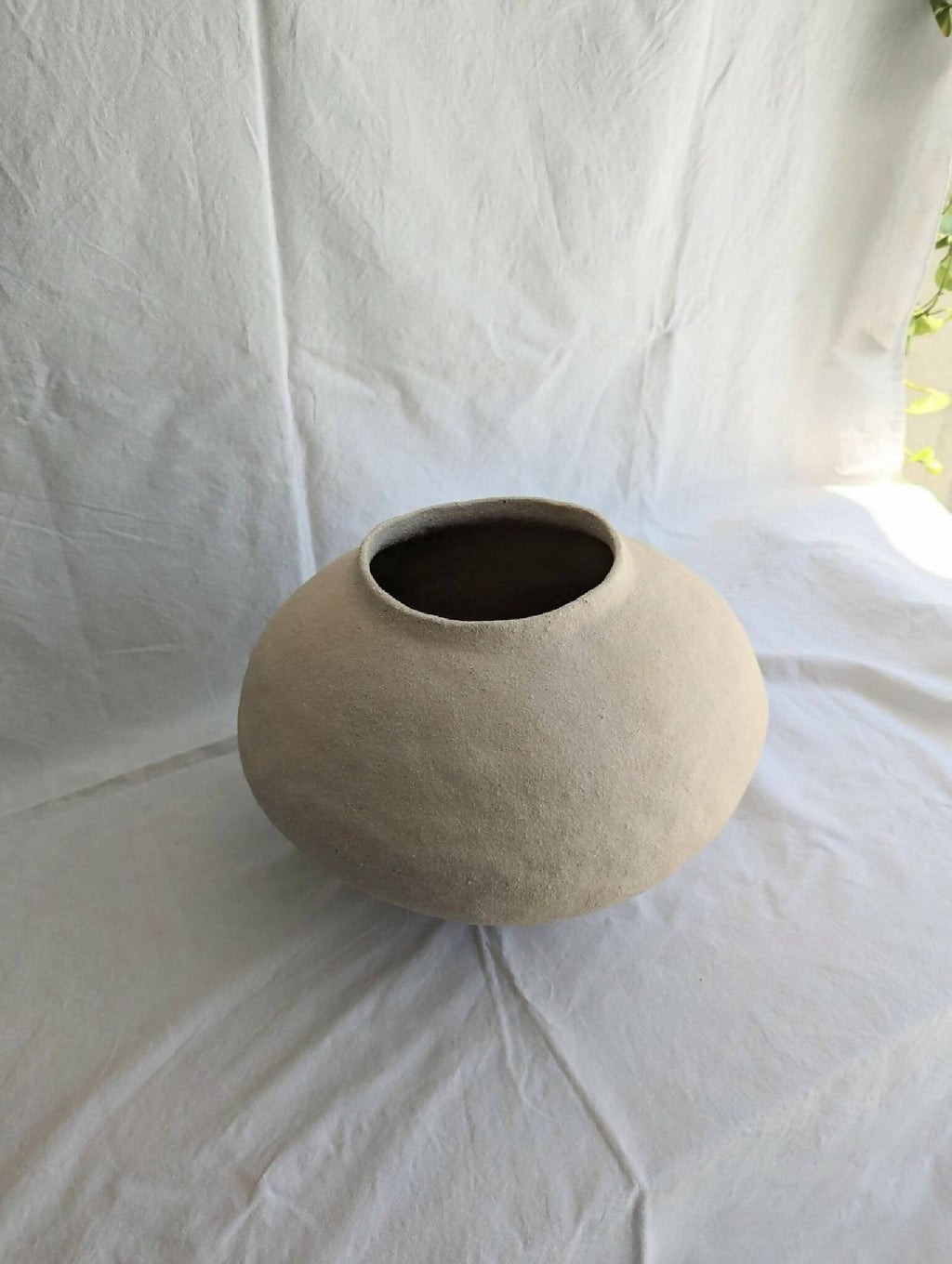 Vase en céramique beige, petit col évasé et intérieur sombre.