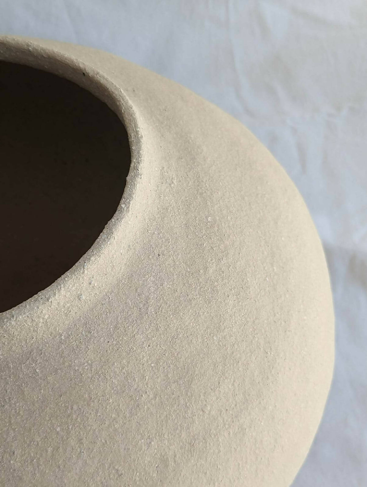 Vase en céramique beige, gros plan sur le bord et la texture mate.