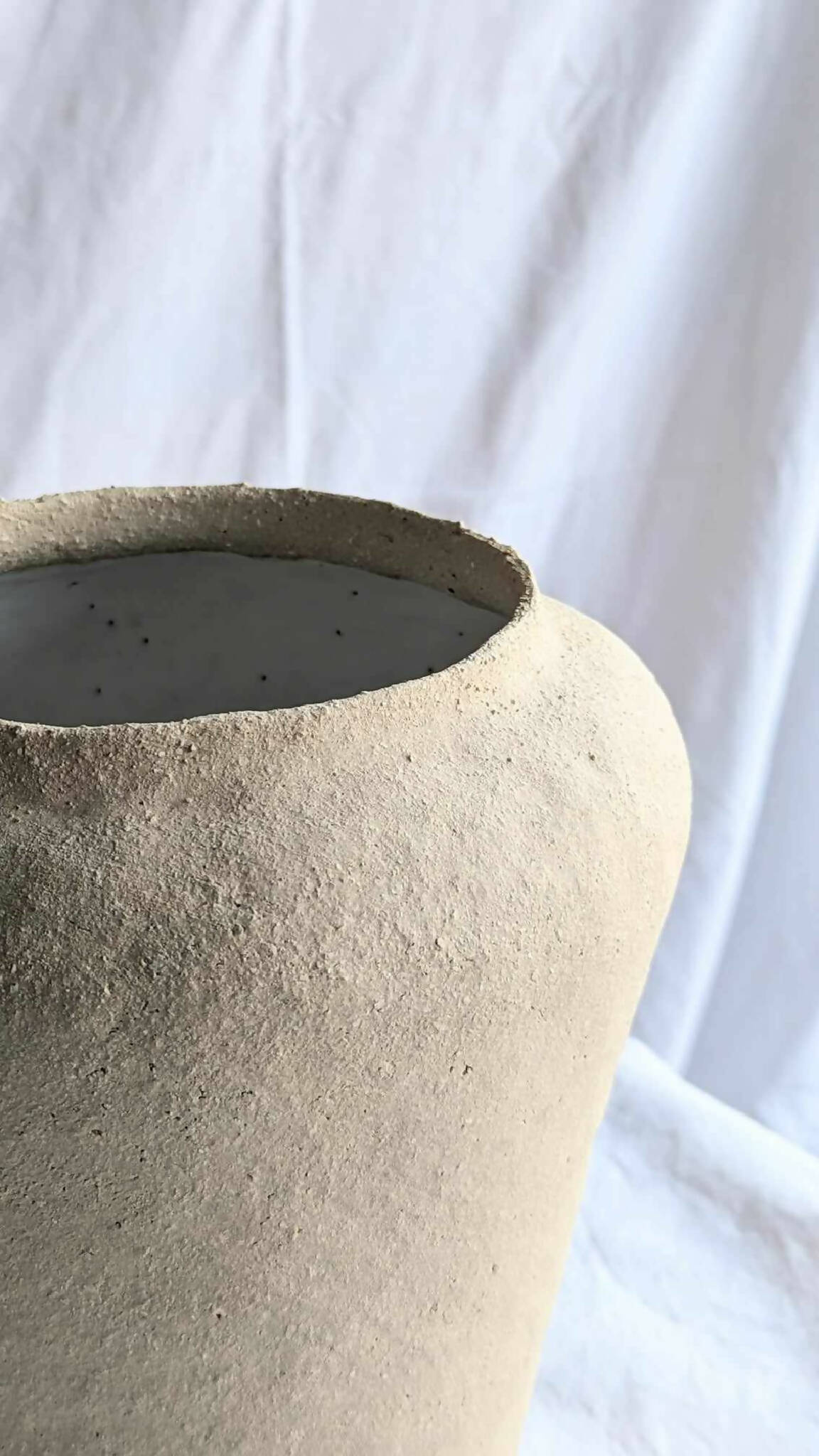 Ouverture du vase conique en céramique beige, bord supérieur foncé.