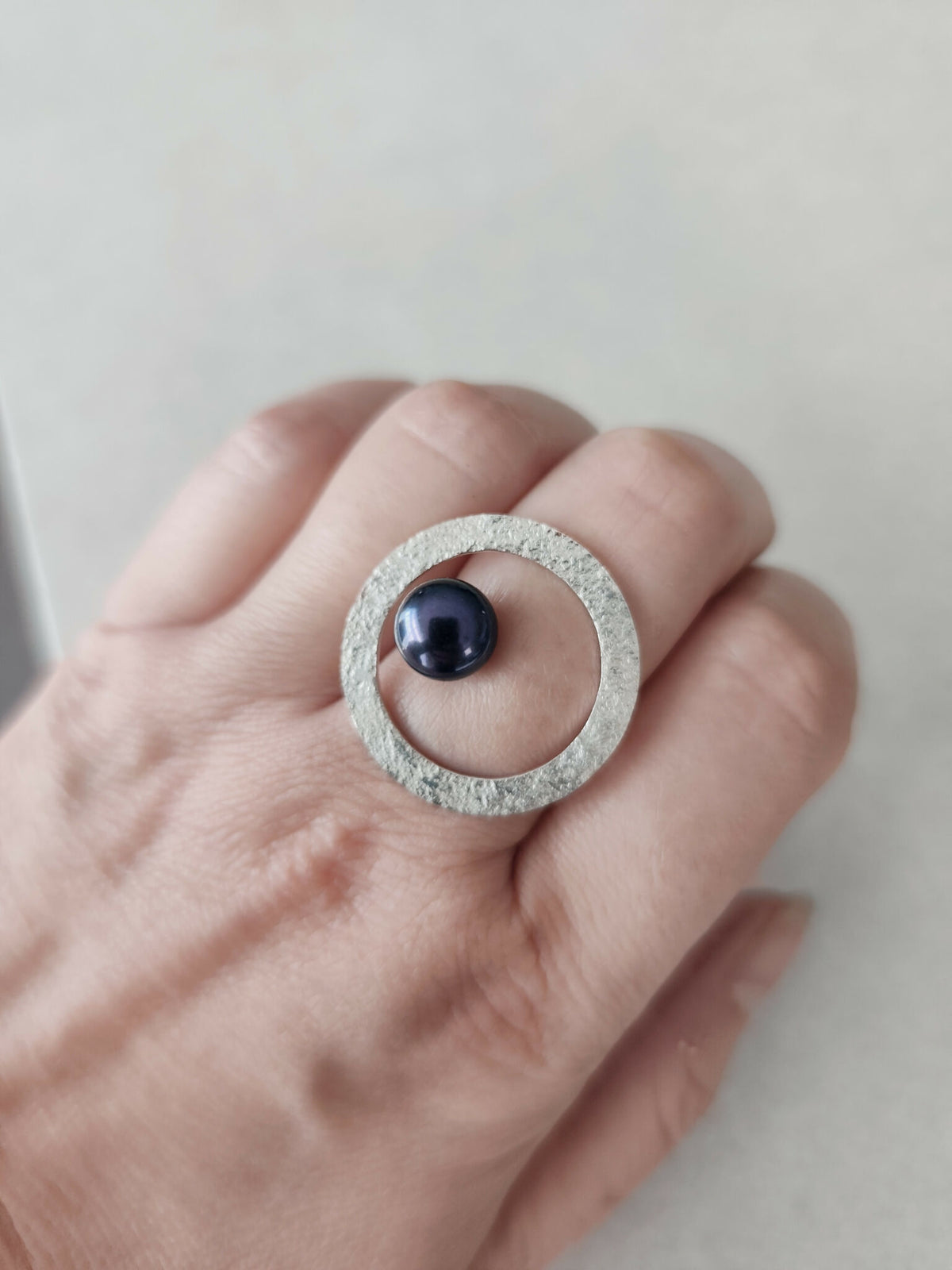 Bague argentée texturée ovale portée, cabochon bleu foncé et anneau visible