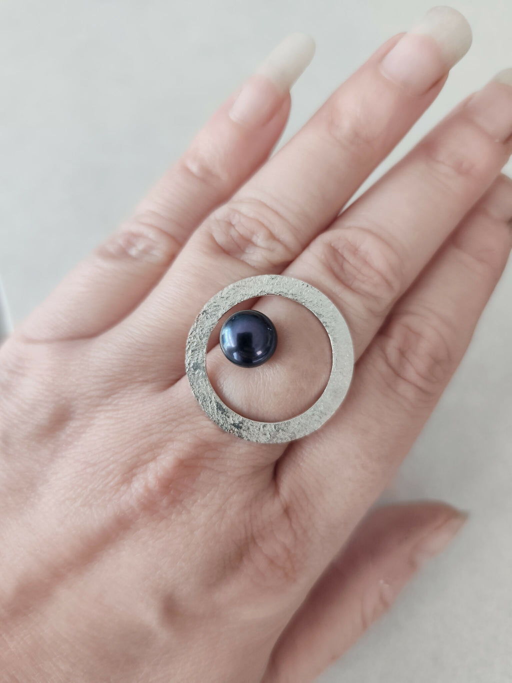Bague ovale argentée texturée sur la main, cabochon bleu foncé bien centré