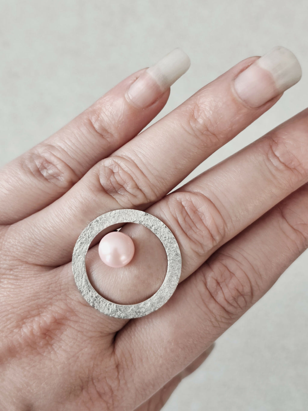 Bague Atoll sur main, cabochon perle rose nacrée dans cercle texturé argenté