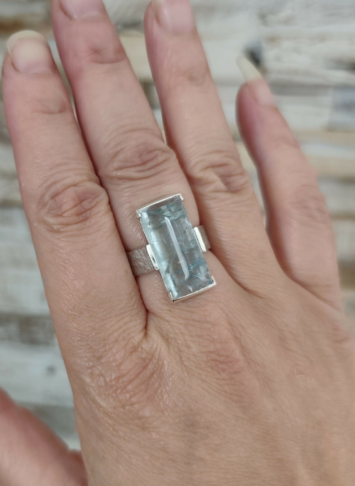 Bague en topaze bleu clair rectangulaire sur la main, monture argent.