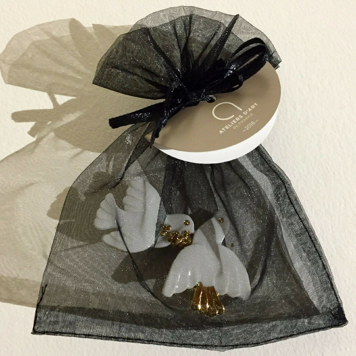 Broche colombes blanches à accents dorés, portée sur sachet en organza.