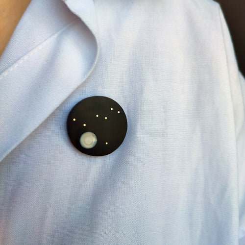 Broche Columba sur chemise claire: cercle noir, ovale clair et points dorés