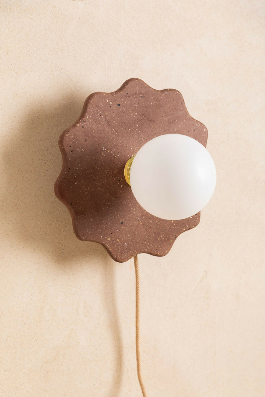 Applique murale en forme de fleur marron foncé, globe blanc avec liseré jaune et câble.