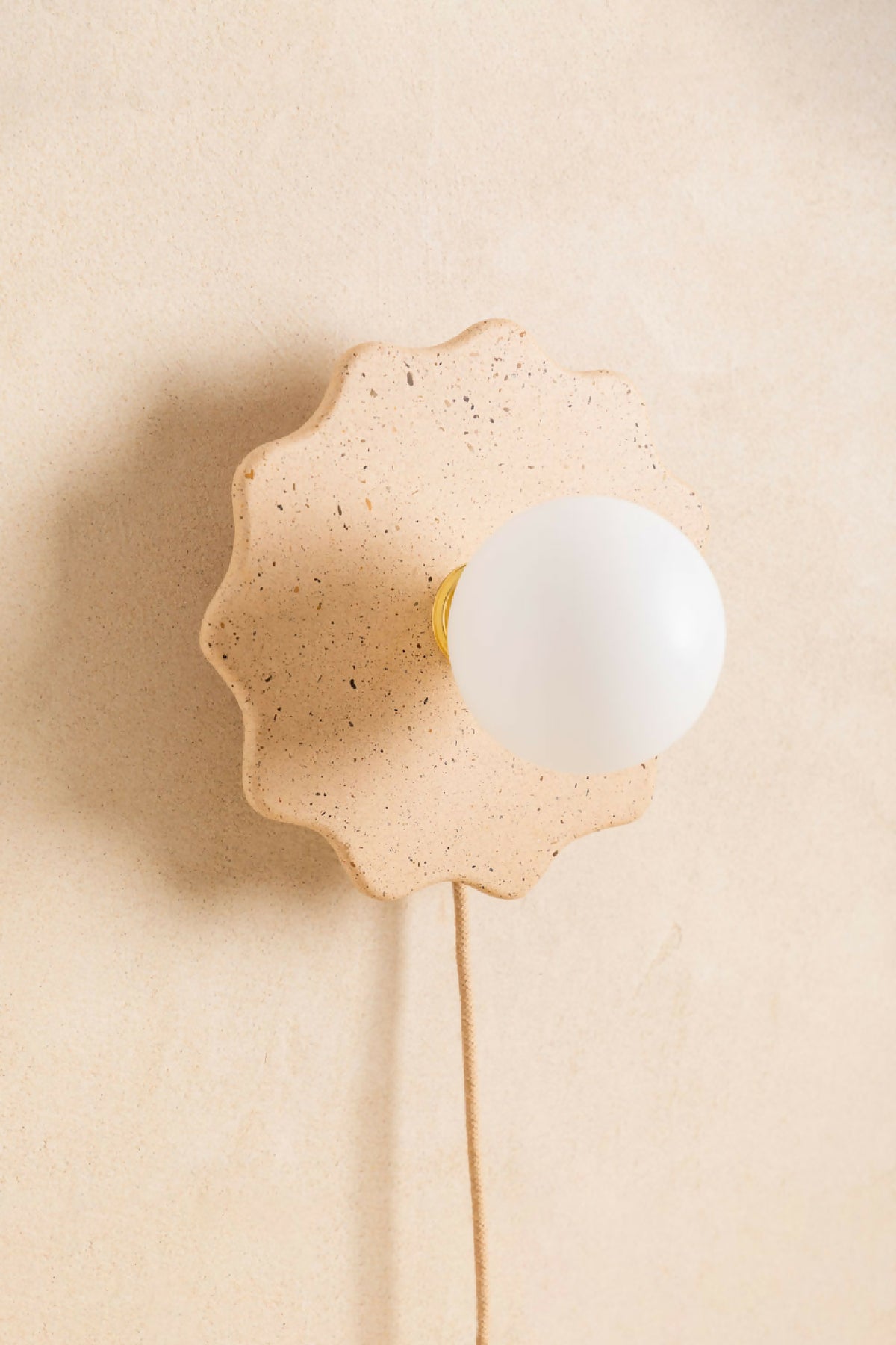 Applique murale en forme de fleur beige clair, globe blanc avec liseré jaune et câble.