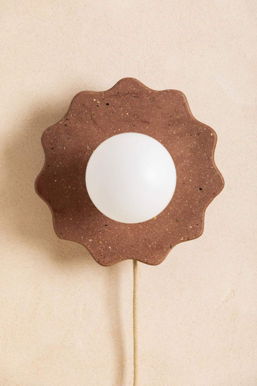Applique murale en forme de fleur marron foncé, globe blanc et câble beige.