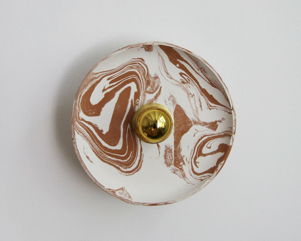 Applique murale ronde marbrée beige et blanc, avec un bouton doré au centre.