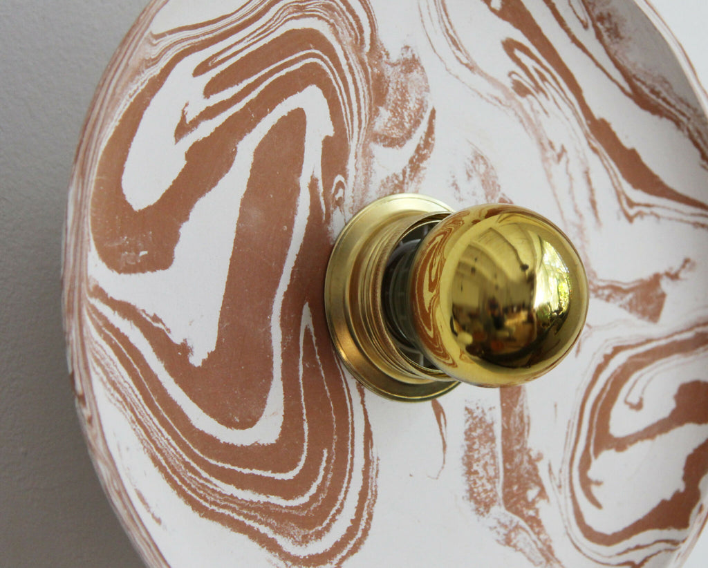 Détail applique murale ronde : boutons dorés sur plaque marbrée beige et blanche.