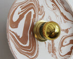 Détail applique murale ronde : boutons dorés sur plaque marbrée beige et blanche.