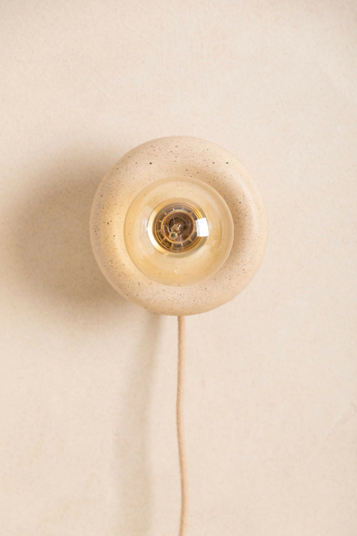 Applique murale ronde beige en verre texturé moucheté, douille centrale dorée, câble visible