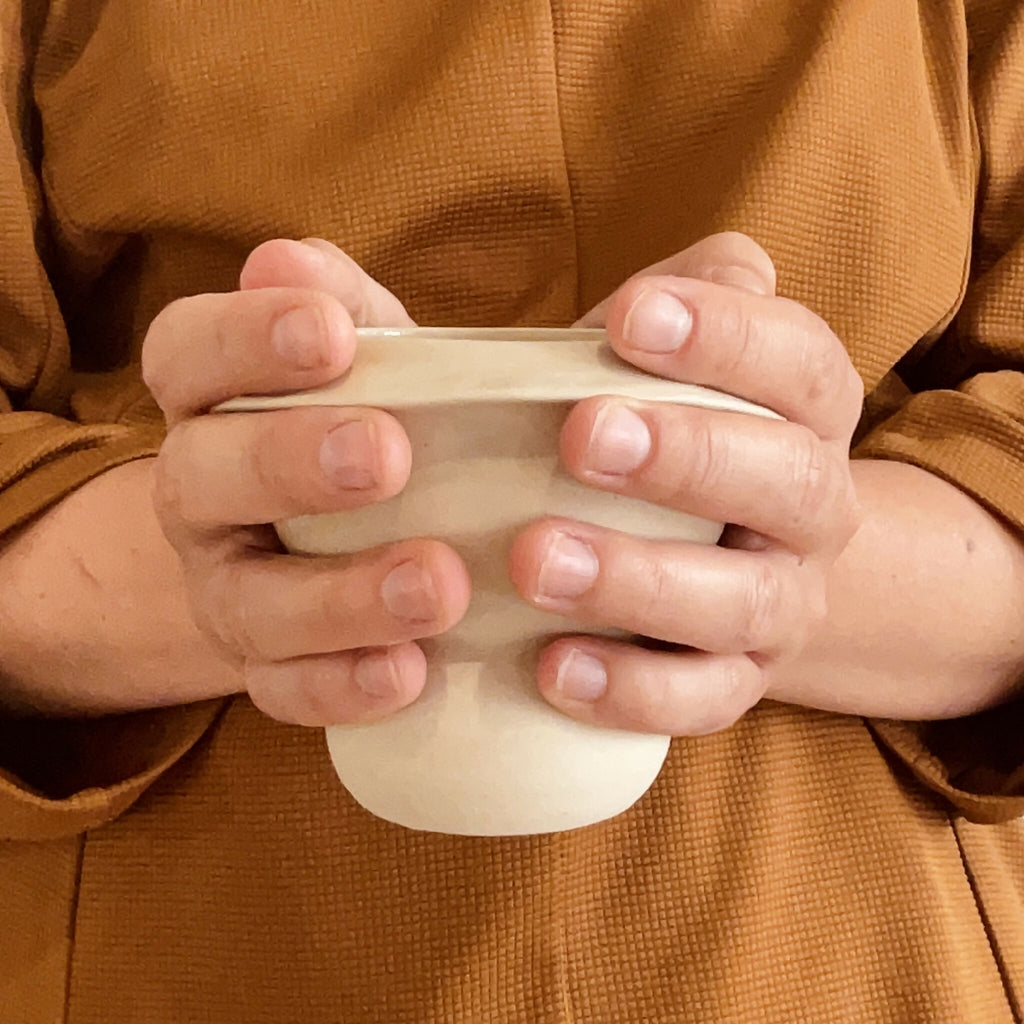 Tasse Bulle en céramique beige, vue rapprochée, tenue par deux mains.