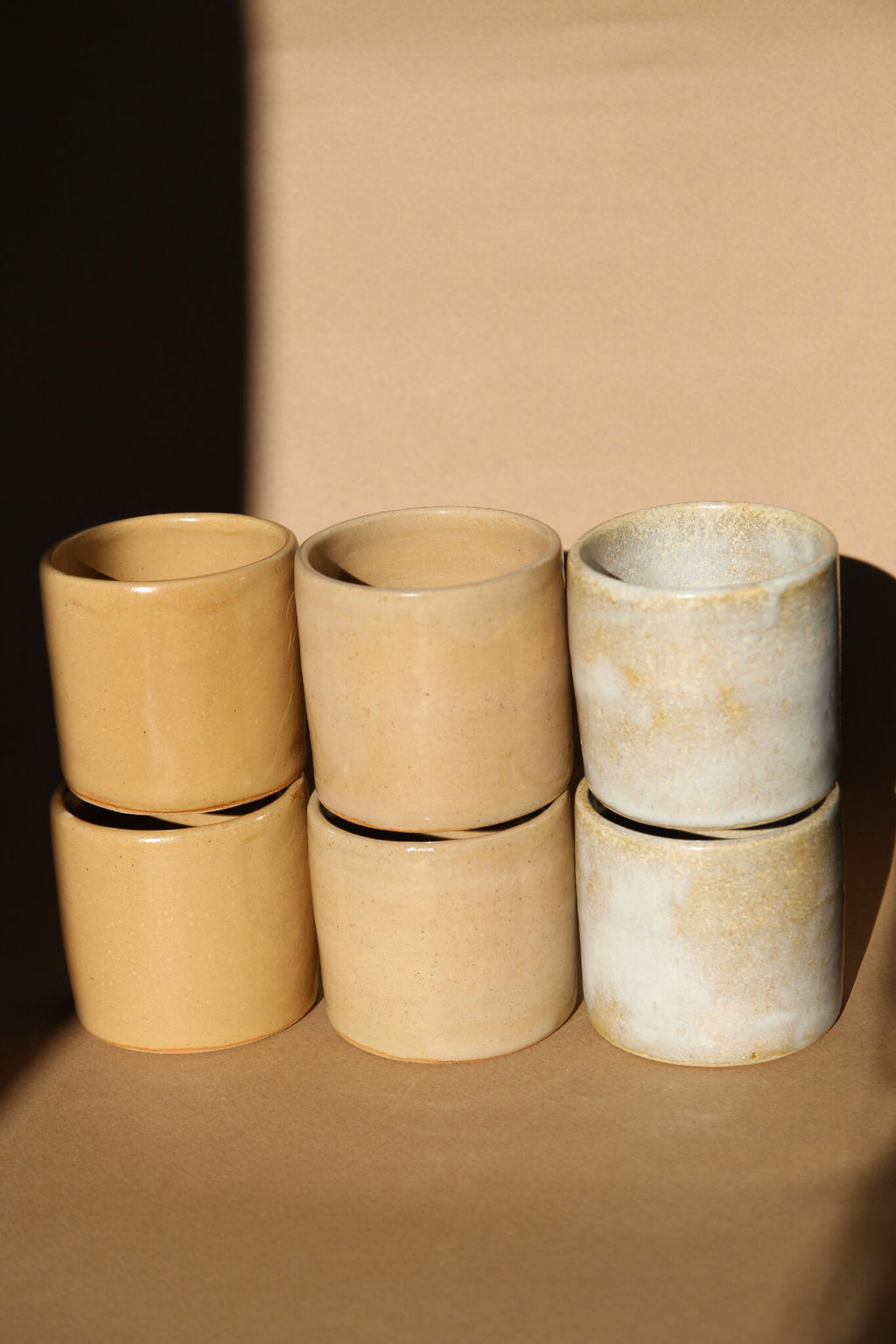 Lot de 6 tasses à expresso en céramique beige et nacrée, empilées par deux.