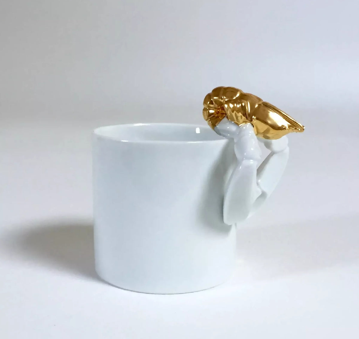 Tasse blanche avec homard doré sur l’anse, vue en légère perspective