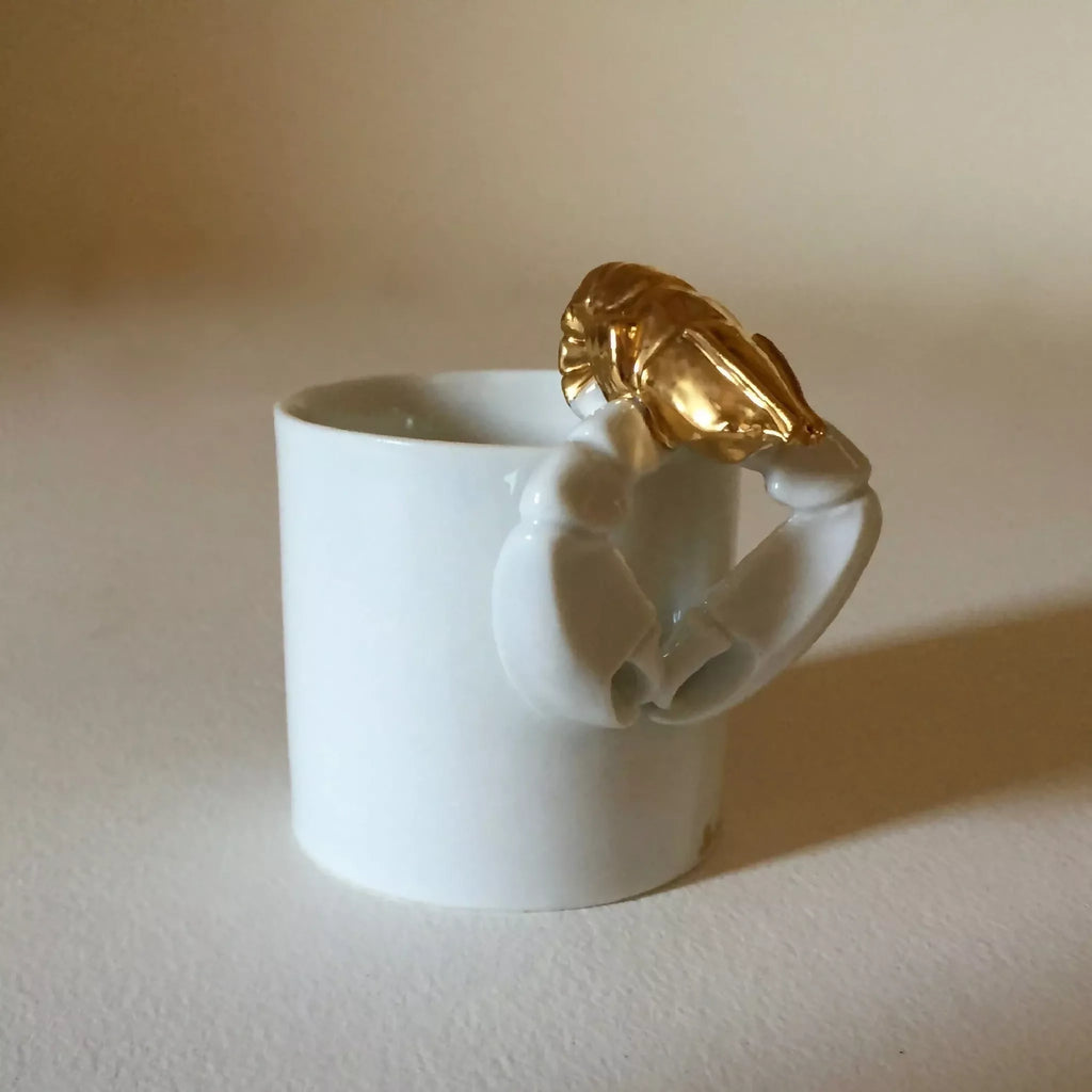 Tasse blanche avec homard doré sur la poignée, vue de trois-quarts