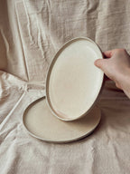 Main tenant une assiette blanche nacrée au-dessus d’une autre, style classique Algue