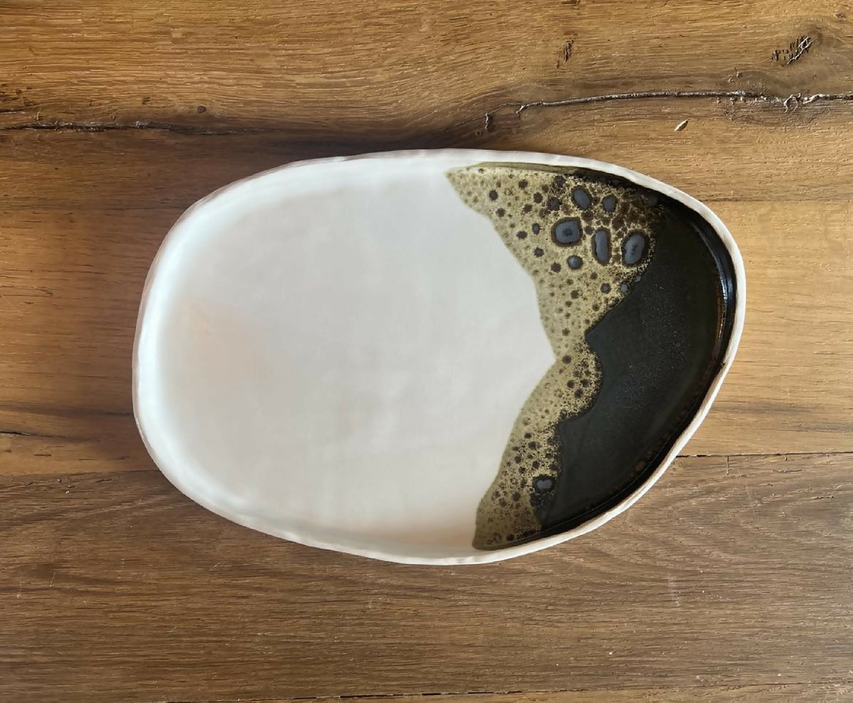 Grande assiette ovale blanche avec zones noir et beige texturées, bord noir