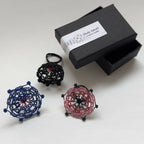 Bague en macramé bleue en forme de trèfle avec centre rose, posée sur des boîtes