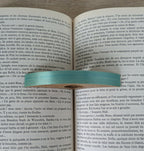 Bague de lecture en bois turquoise, insérée dans un livre, vue rapprochée