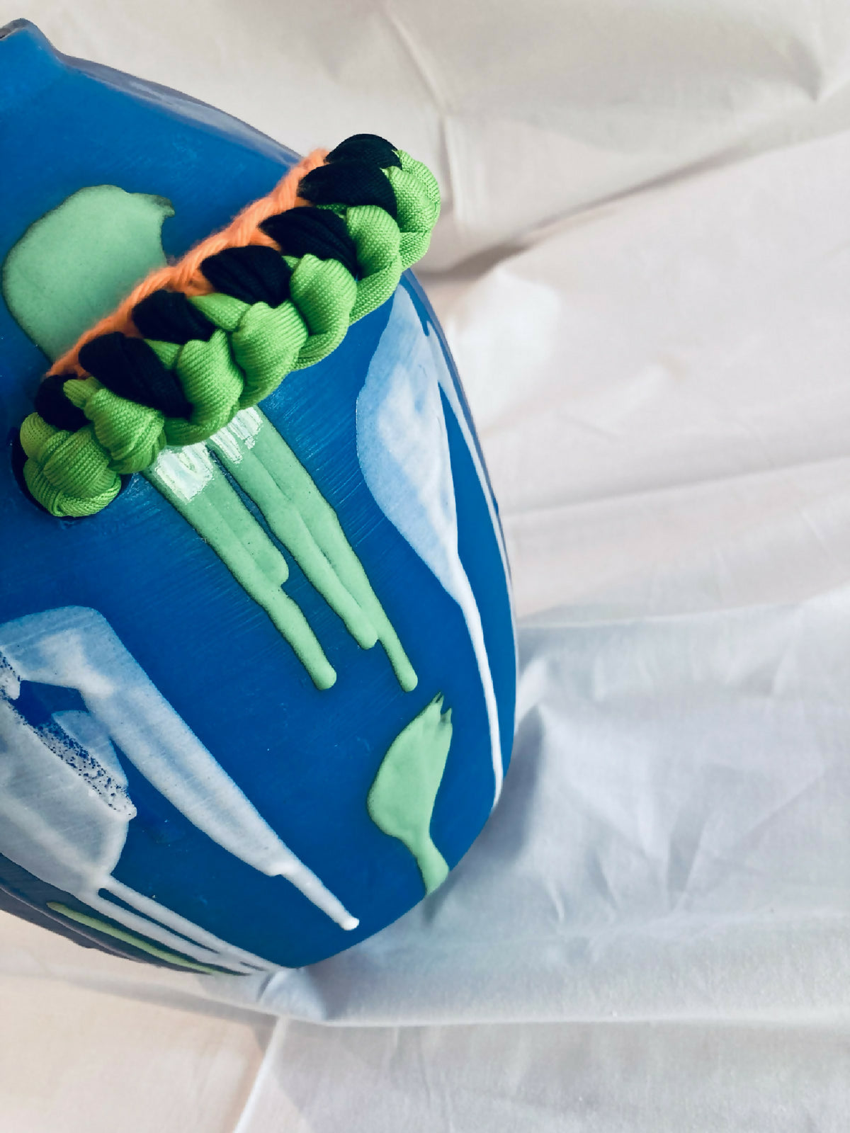 Vase amphore bleu avec détail tressé vert et orange, motif vert vertical sur le côté.