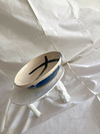 Bol en grès blanc avec motif bleu en croissant, vue en biais sur pied.