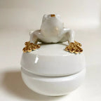 Boîte à bijoux grenouille blanche debout sur un socle, détails dorés sur les pattes.