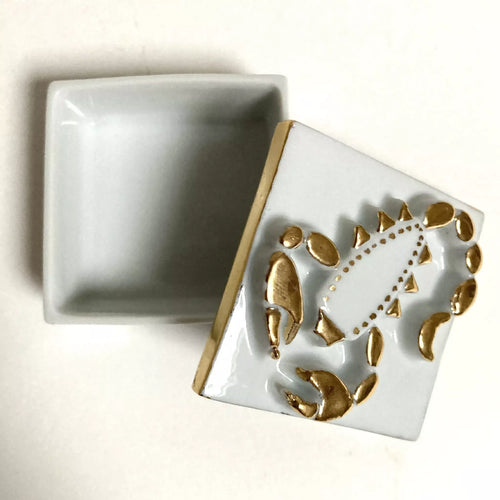 Boîte à bijoux en porcelaine carrée, couvercle ouvert, motif scorpion doré sur fond clair.