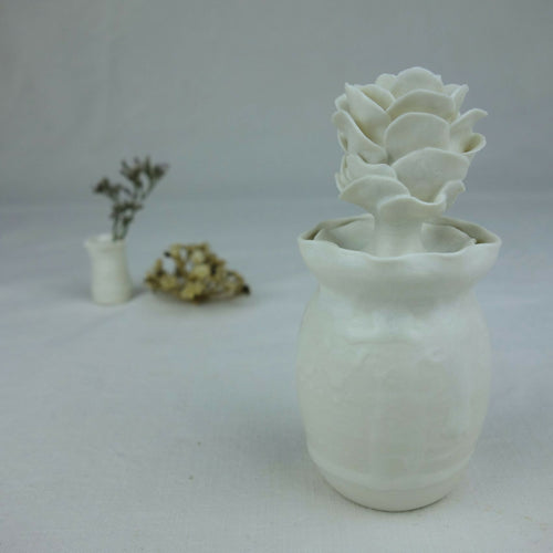 Vase en céramique blanc avec fleurs en relief empilées au centre, vue de profil.