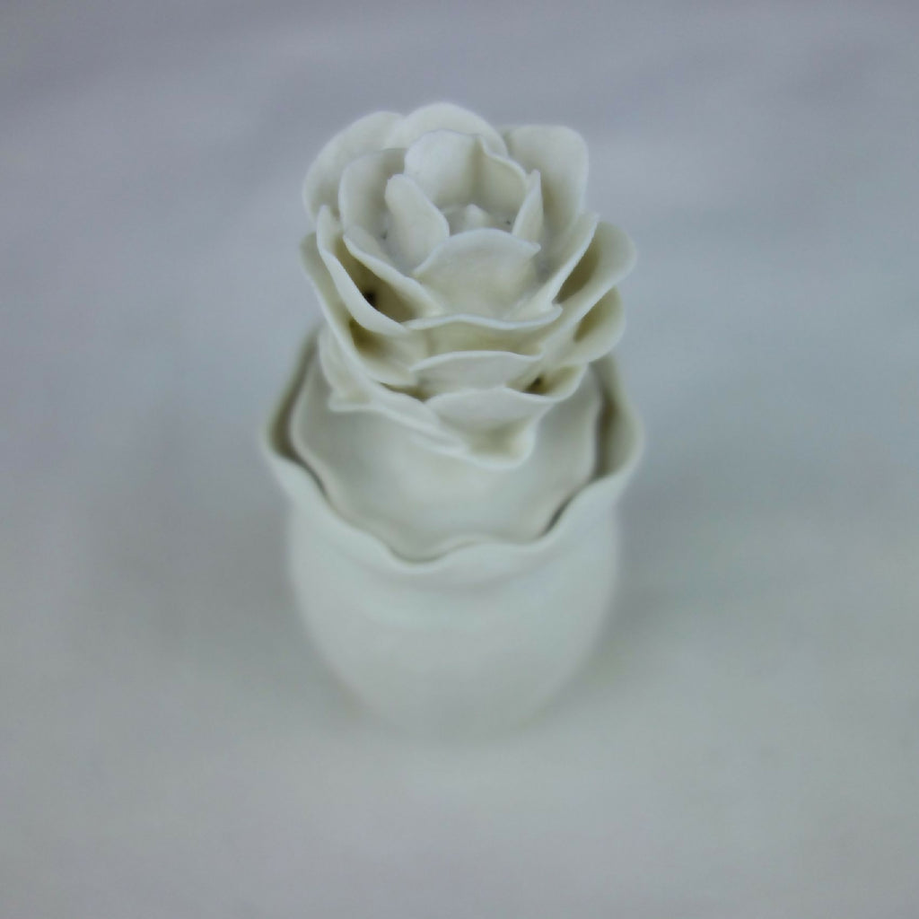 Vase en céramique blanc, fleurs en relief empilées, vue inclinée rapprochée.