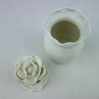 Vase en céramique blanc avec ouverture supérieure; petite fleur en relief à côté.