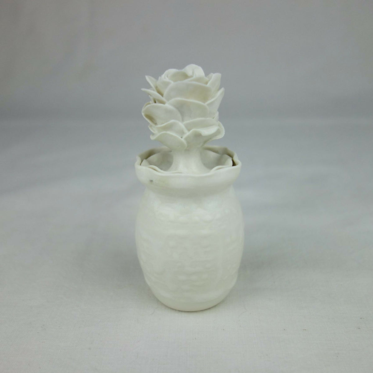 Vase en céramique blanc, fleurs en relief au sommet, vue entière centrée.
