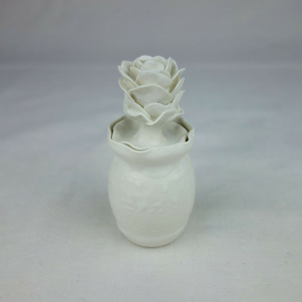 Vase en céramique blanc avec décoration florale en relief, vue de face légère.