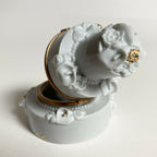 Boîte en porcelaine blanche ouverte, gros plan sur décor floral et accent doré.