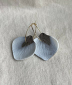 Boucles d’oreille créoles en porcelaine, pétales bleu ciel et détails sombres.