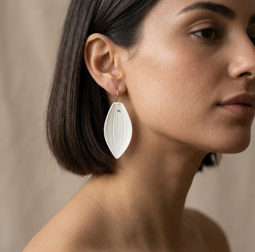 Boucles d’oreille en porcelaine blanche ovales, portées, sur tige dorée.
