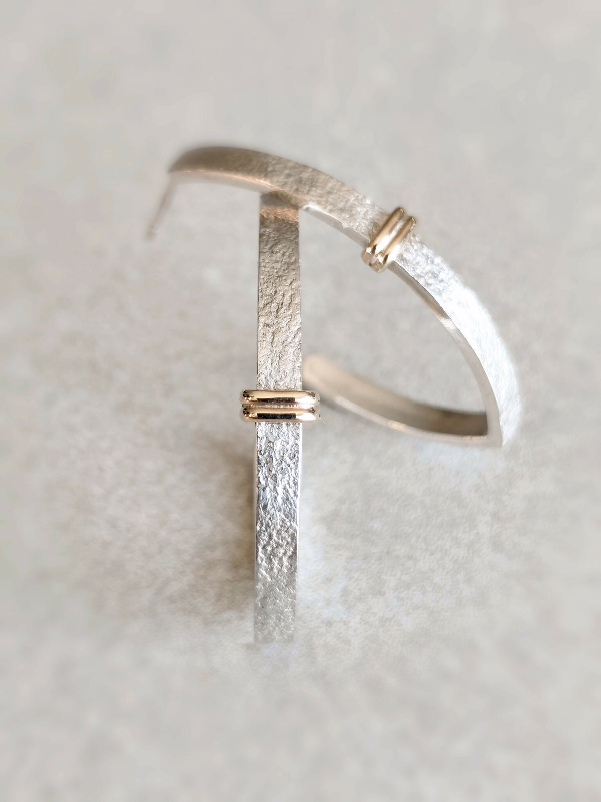 Boucle d’oreille courbe argentée texturée avec fermoir doré, vue rapprochée