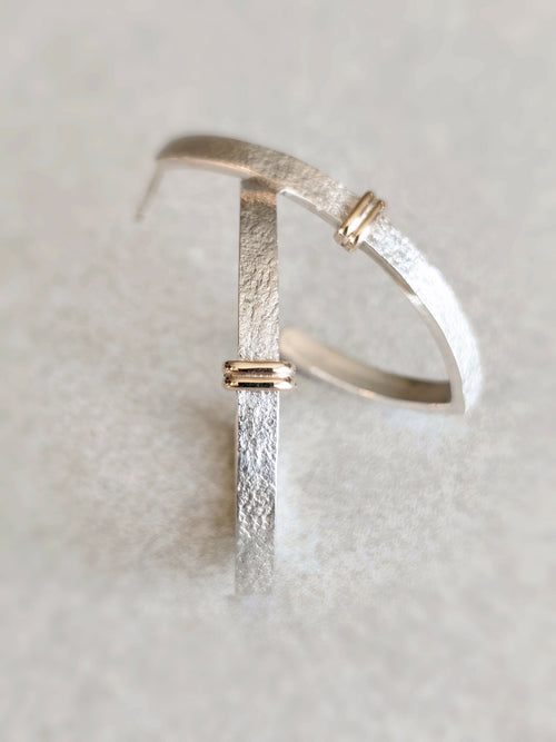Boucle d’oreille courbe argentée texturée avec fermoir doré, vue rapprochée