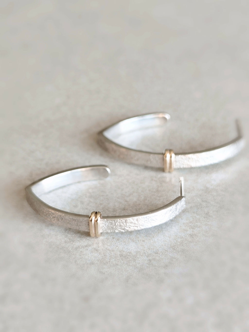 Boucles d’oreilles courbes argentées brillantes avec anneaux dorés sur la jonction