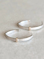Boucles d’oreilles courbes argentées brillantes avec anneaux dorés sur la jonction