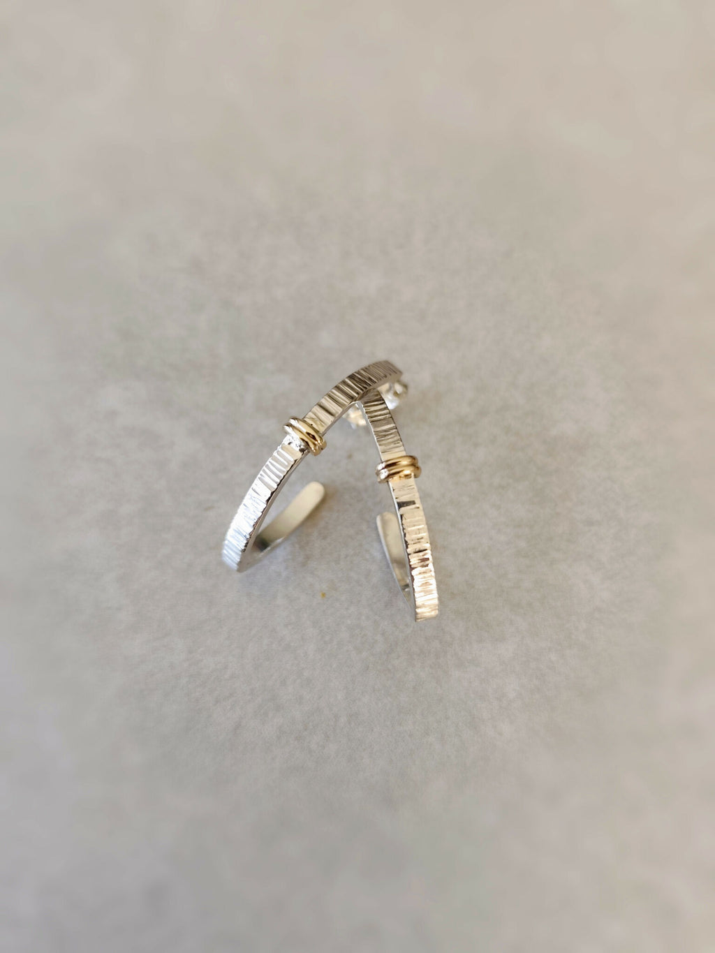 Boucles d’oreilles courbées argentées, rayures fines et accents dorés, vue rapprochée