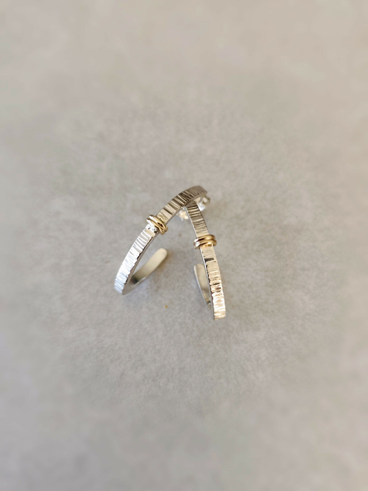Boucles d’oreilles courbées argentées, rayures fines et accents dorés, vue rapprochée