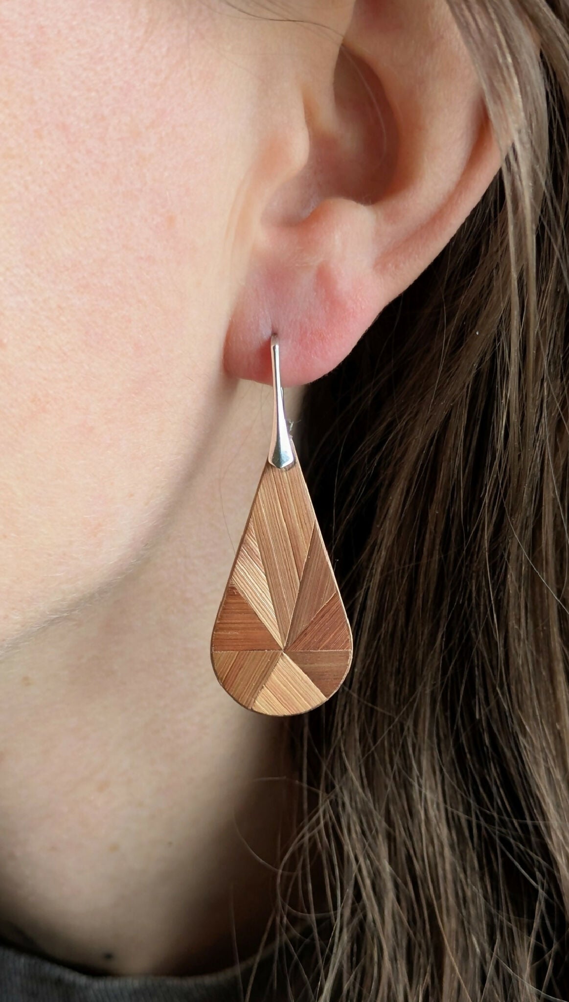 Boucle d’oreille goutte en marqueterie bois cuivré, crochet argent, portée sur l’oreille.