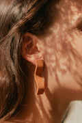 Boucles d’oreilles pendantes en barres courbées couleur terre cuite, gros plan à l’oreille