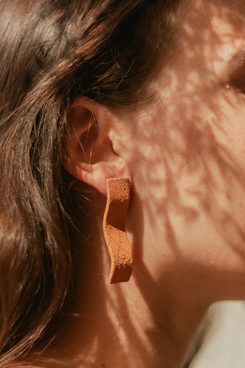 Boucles d’oreilles pendantes en barres courbées couleur terre cuite, gros plan à l’oreille