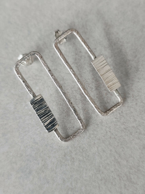 Boucles d’oreilles rectangulaires argentées, gros plan des textures à rayures.