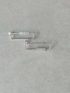 Boucles d’oreilles rectangulaires argentées, détail des fermoirs et des rayures.